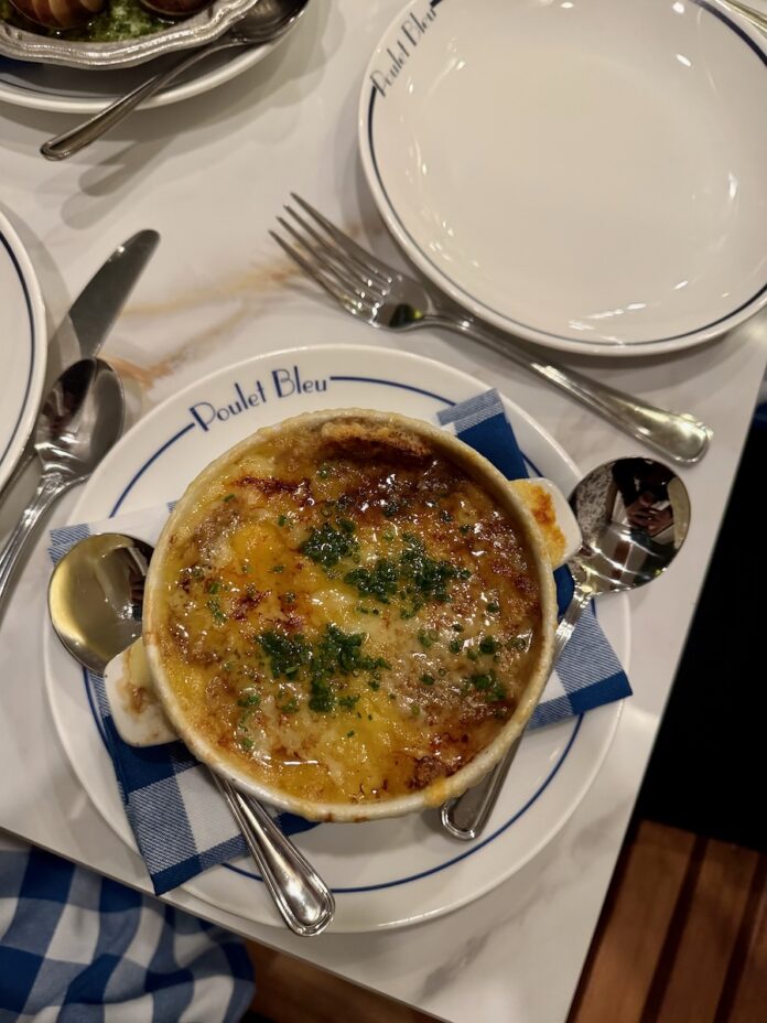 A bowl of soup with herbs and noodles all on a white place setting.