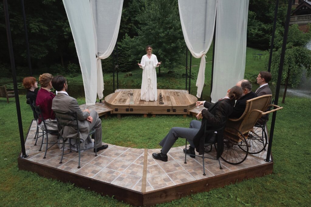A group of people sitting around an outdoor deck with a woman in white in middle. 