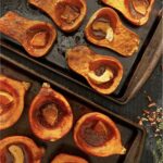 A variety of roasted squash on a baking sheet filled with orange slices and spices.
