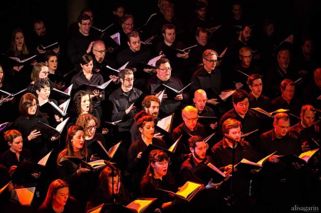 A large choir sings together holding music in binders.
