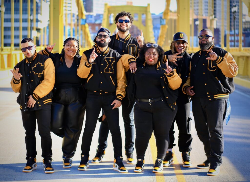 A group of 1HOOD Media members in black and yellow jackets on a bridge.