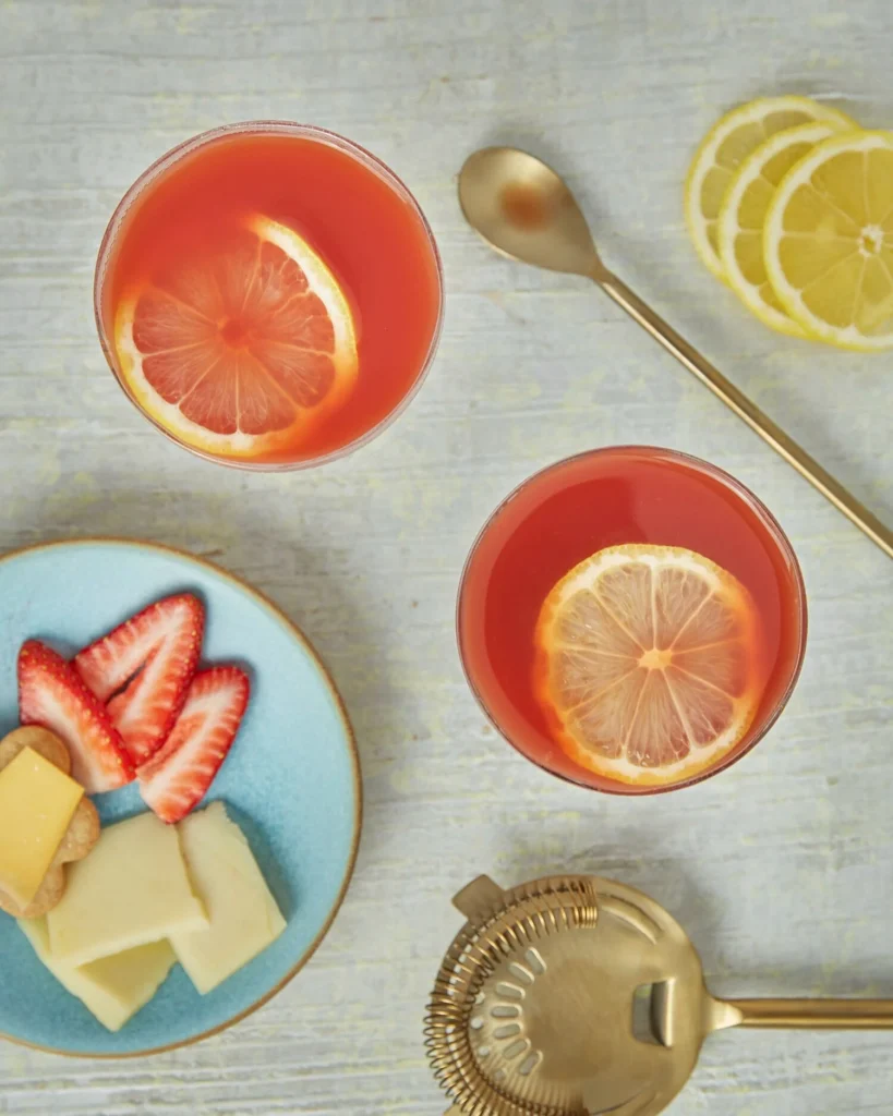 An above shot of two Aperol sour cocktails, light red in color, garnished by lemon slices.