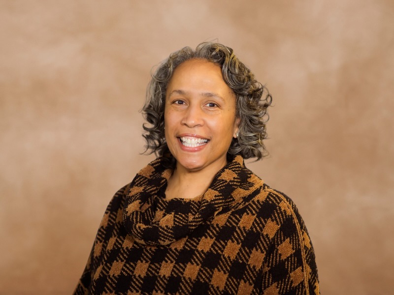 A woman stands against a brown wall with a flannel on.