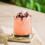 Blackberry Penicillin with cherry garnish and greenery in the background