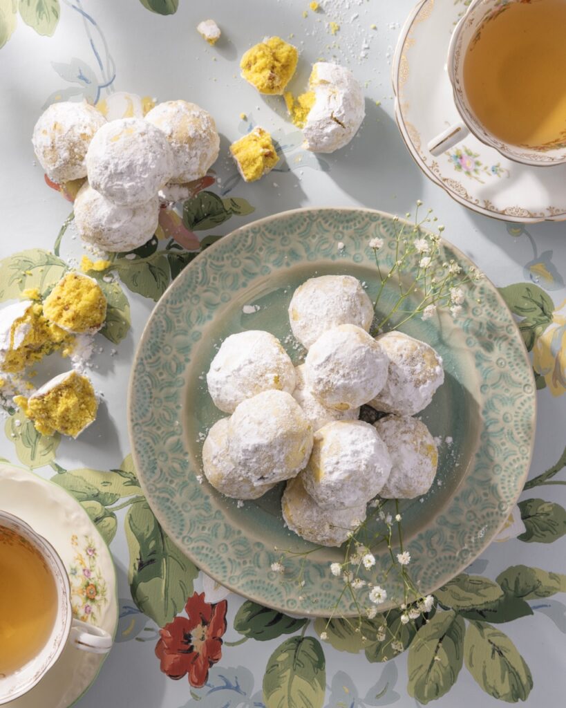 A green plate full of Pecan Balls stacked in a tower as some sit open with yellow cake on the table.