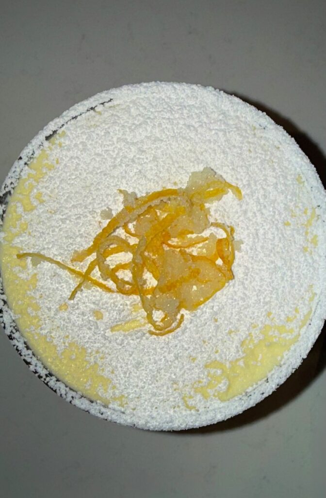 A dessert in a glass with candied lemon and powdered sugar on top.