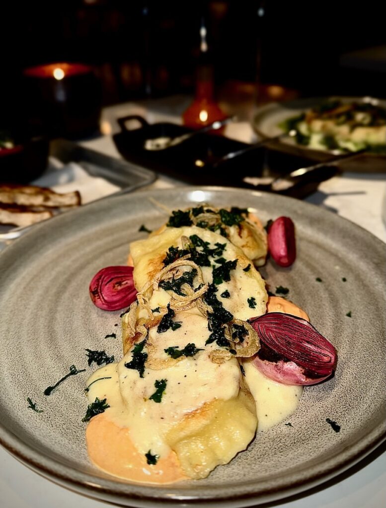 Pierogis in an orange sauce sit on a plate with purple onions.