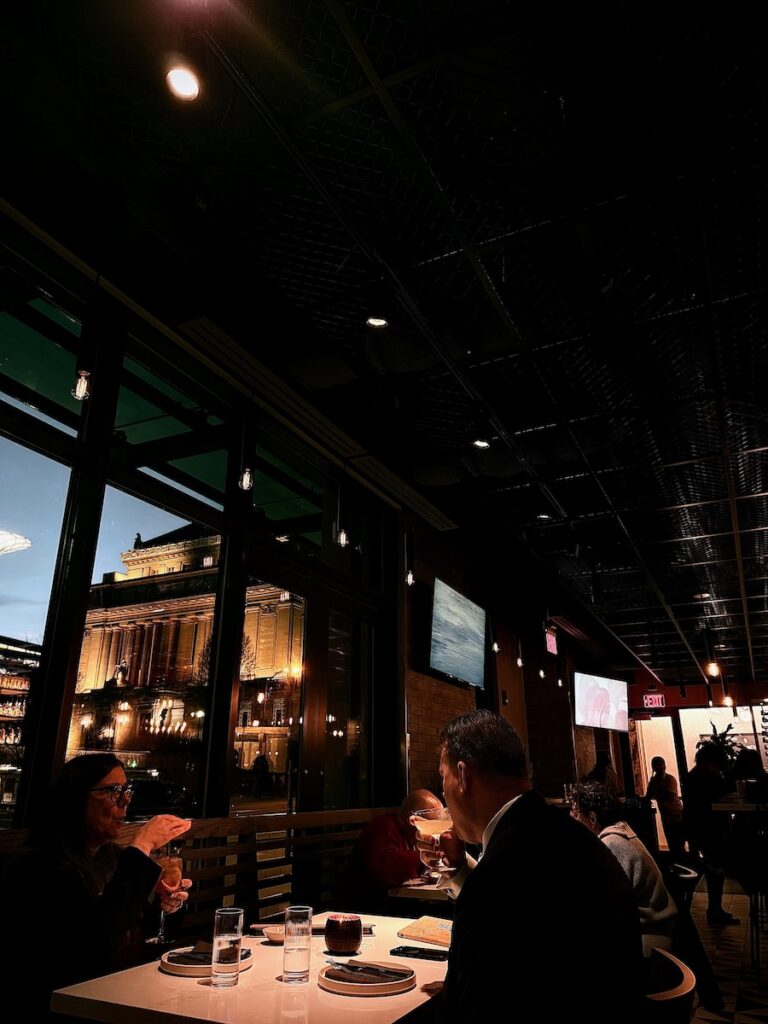 People sit at a table in a low-lit restaurant beside windows.