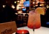 Cork & Crust New Italian Restaurant Opens in The Oaklander Hotel An orange cocktail sits beside a candle and Cork & Cork menu on a white table.