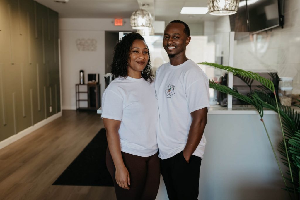 A man and woman stand in white shirts in a juice shop.