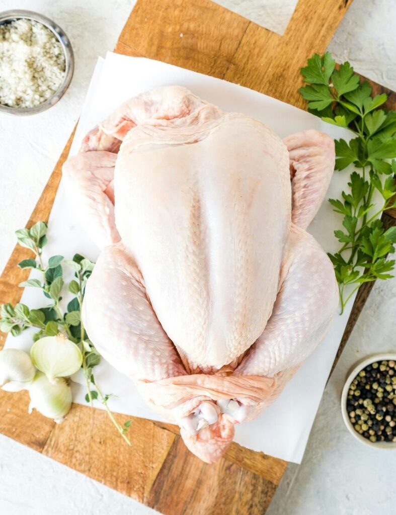 An uncooked chicken sits on a cutting board.