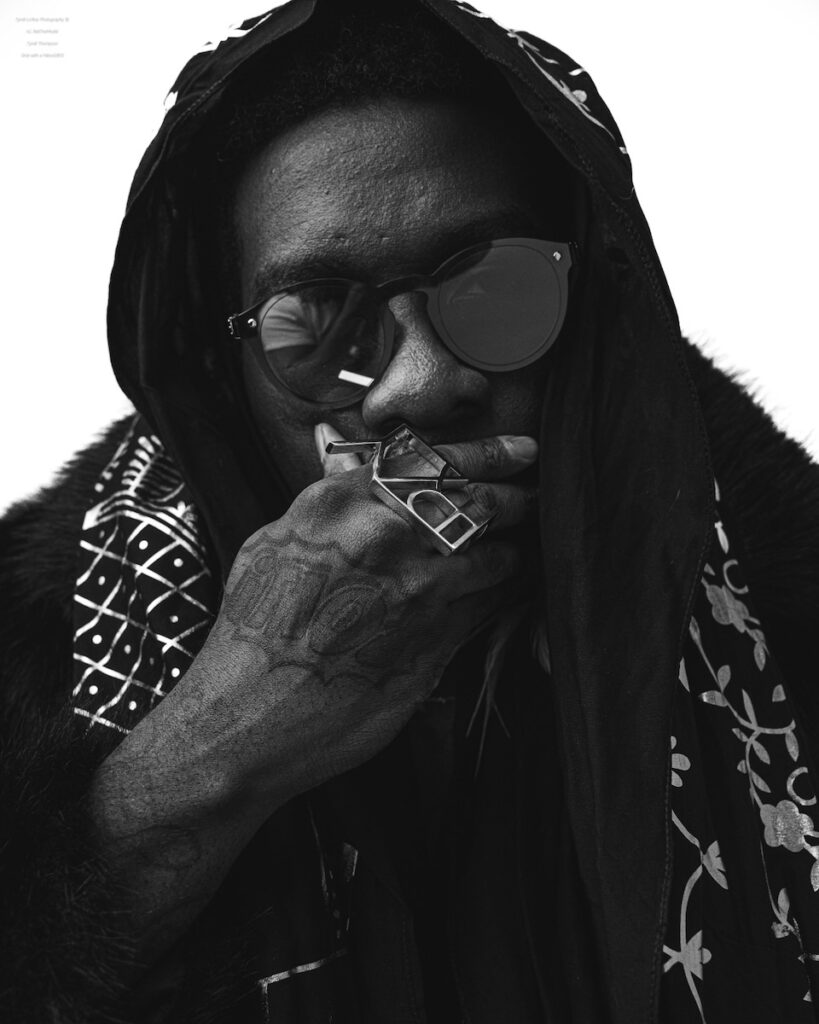 Frzy sits in black and white in front of a white background with sunglasses on.
