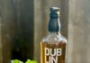 Armchair Quarterback Cocktail A copper mug with a cocktail garnished with fresh mint next to a bottle of Dubliner Steelers Select Irish Whiskey on a brown wood surface.