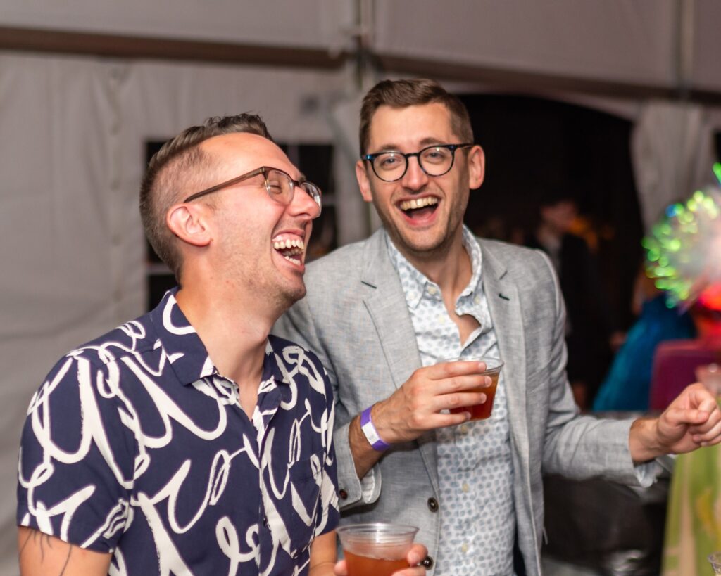 Two men smile and sip on drinks together