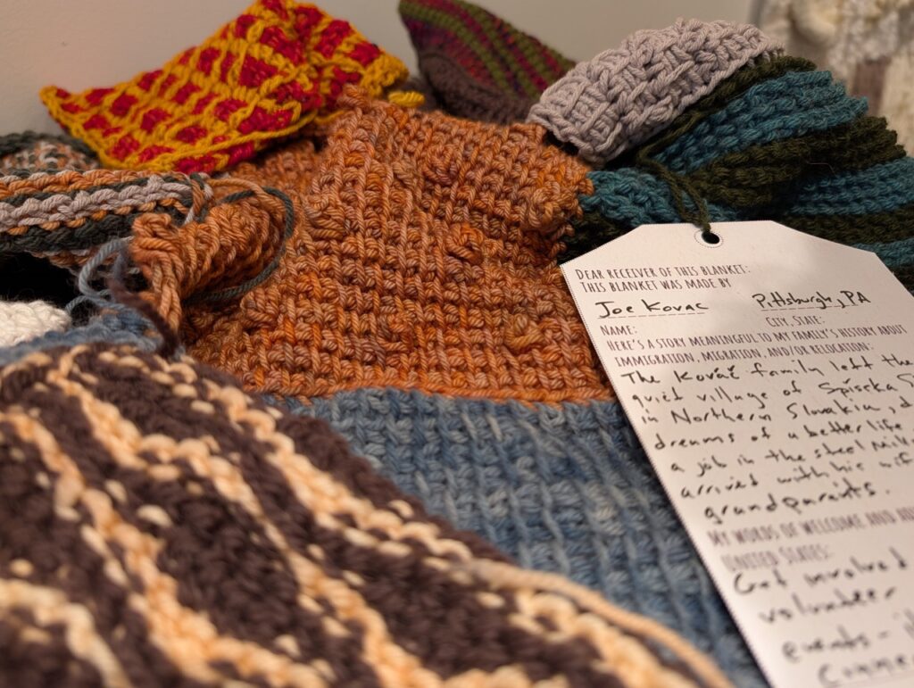 Knit square pieces of various colors stacked on top of each other with tags hanging from them.