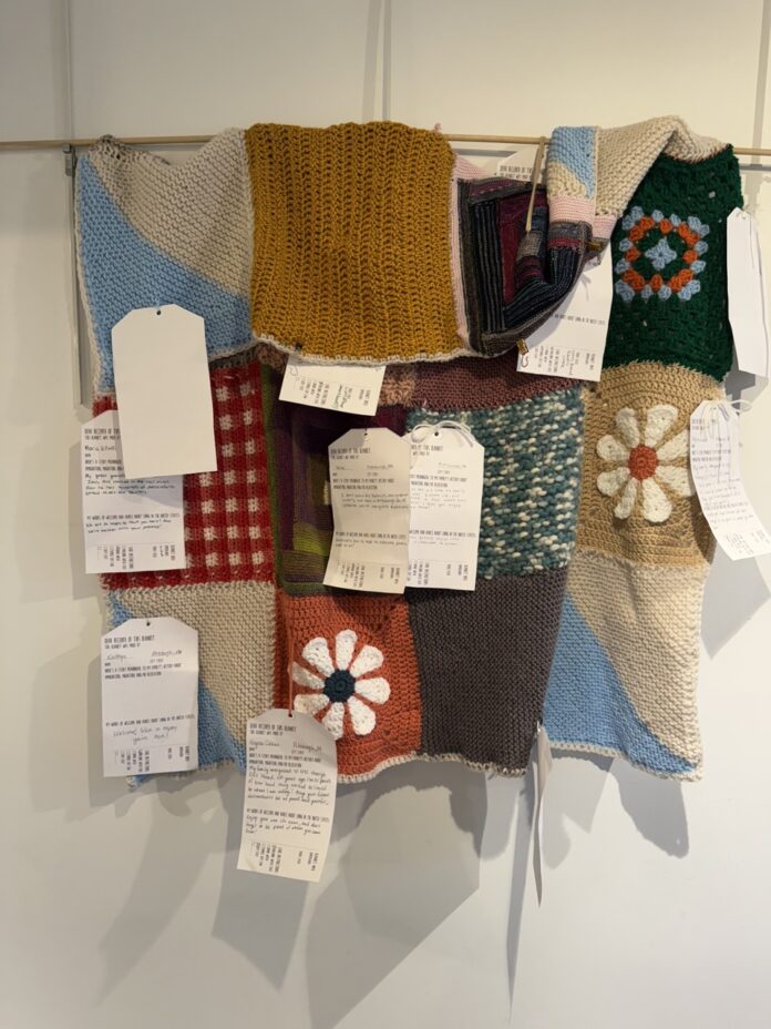 Scraps of various knit squares hang on a wall.