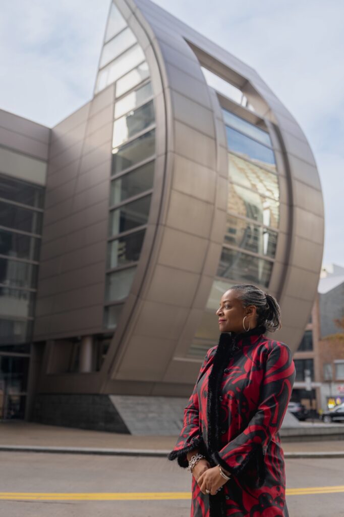 A woman in a long red jacket stands in front of a building.