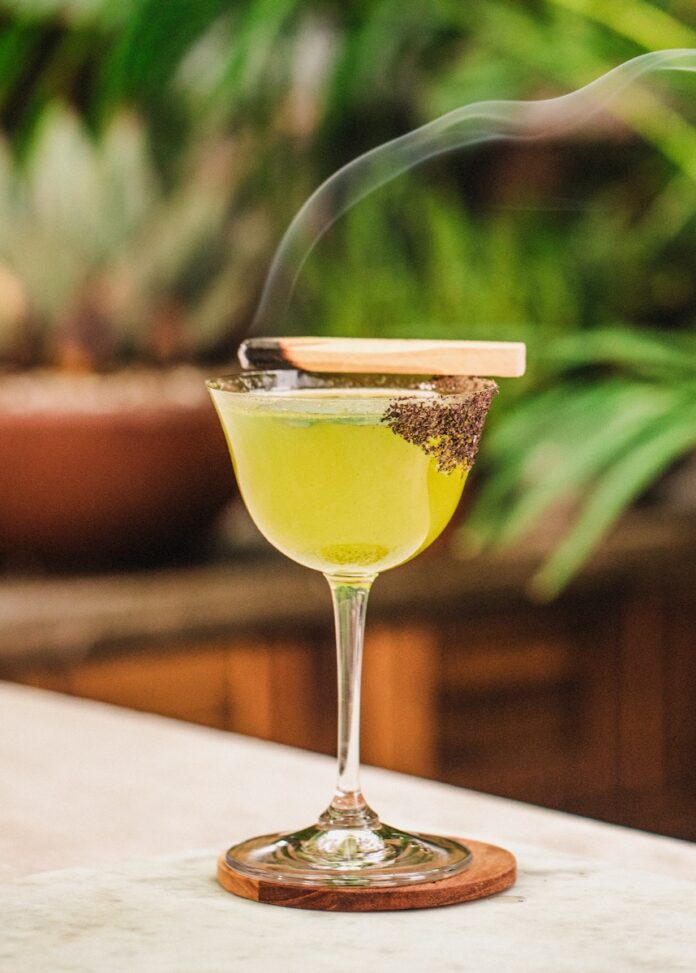 Margarita Verde with smoking wood as garnish greenery in the background