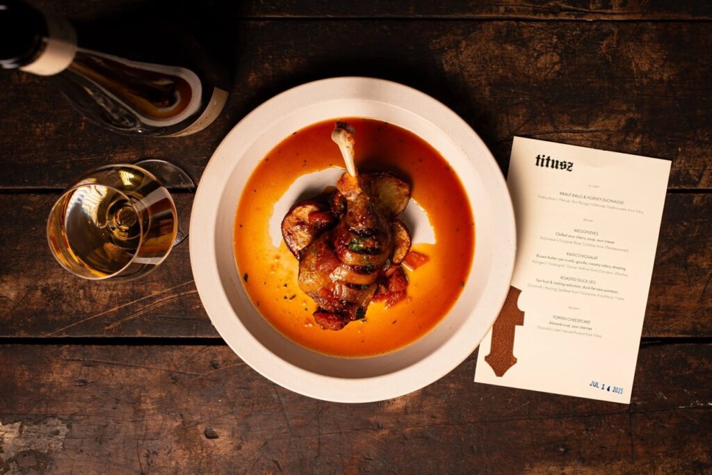 A plate of chicken in between a glass of wine and restaurant menu.