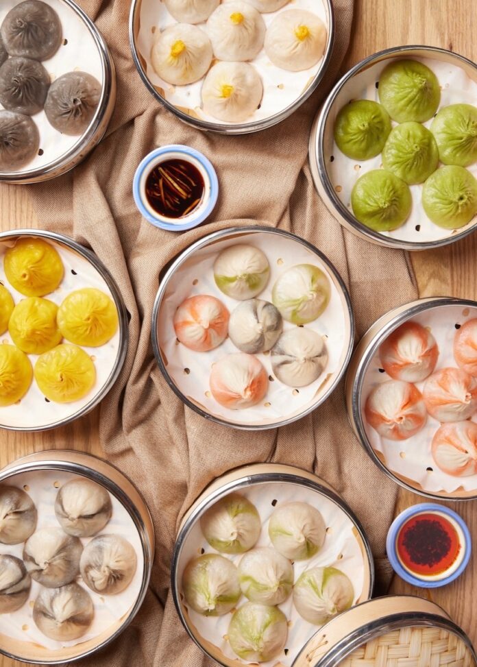 Plates of soup dumplings on a restaurant table with sauces around them too.