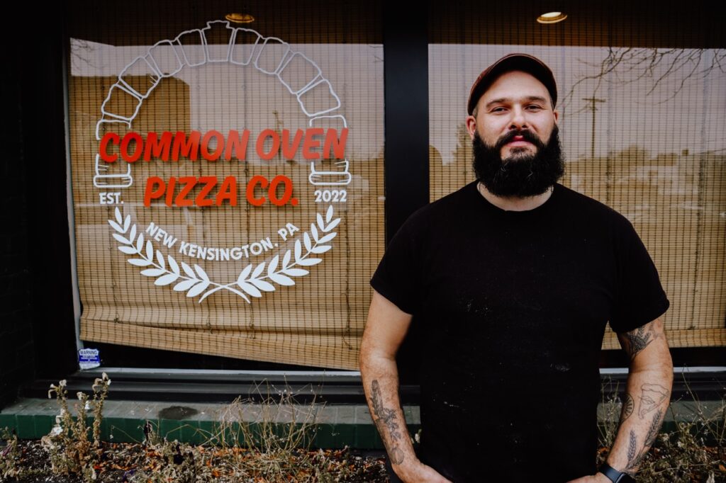 A man stands in front of the window for Common Oven Pizza in New Kensington.