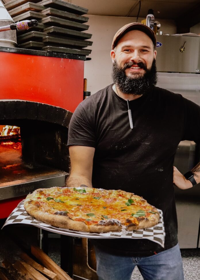 A man holds a cooked pizza out in front of him.