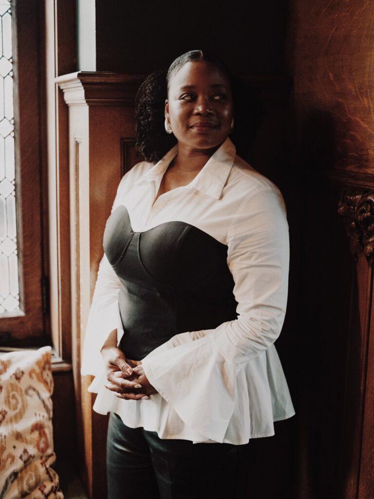 A woman in a white and black top against a wood wall.