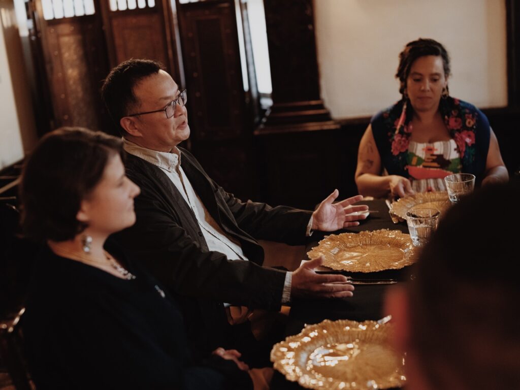A man in a black suit jacket talks to others at a table.