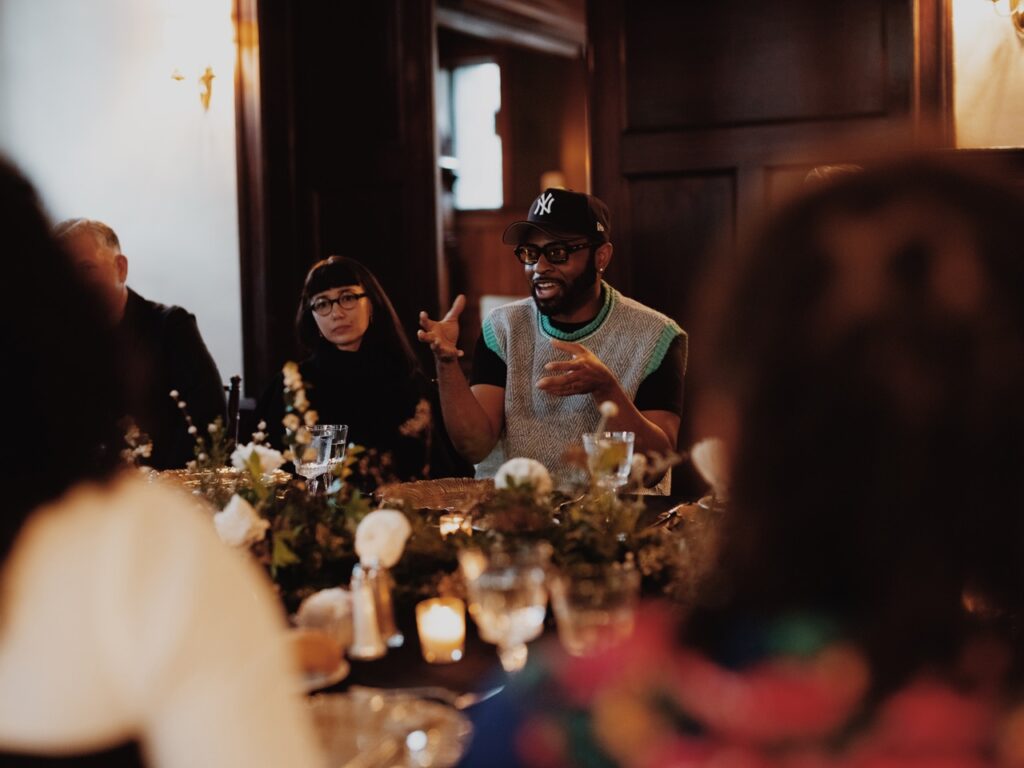 A man in a baseball hat talks to others at a table.