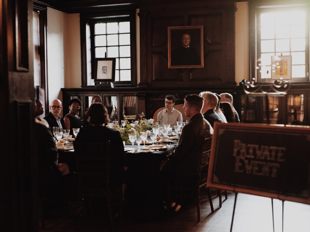 A group of artists leaders sit together at a wood dining table.