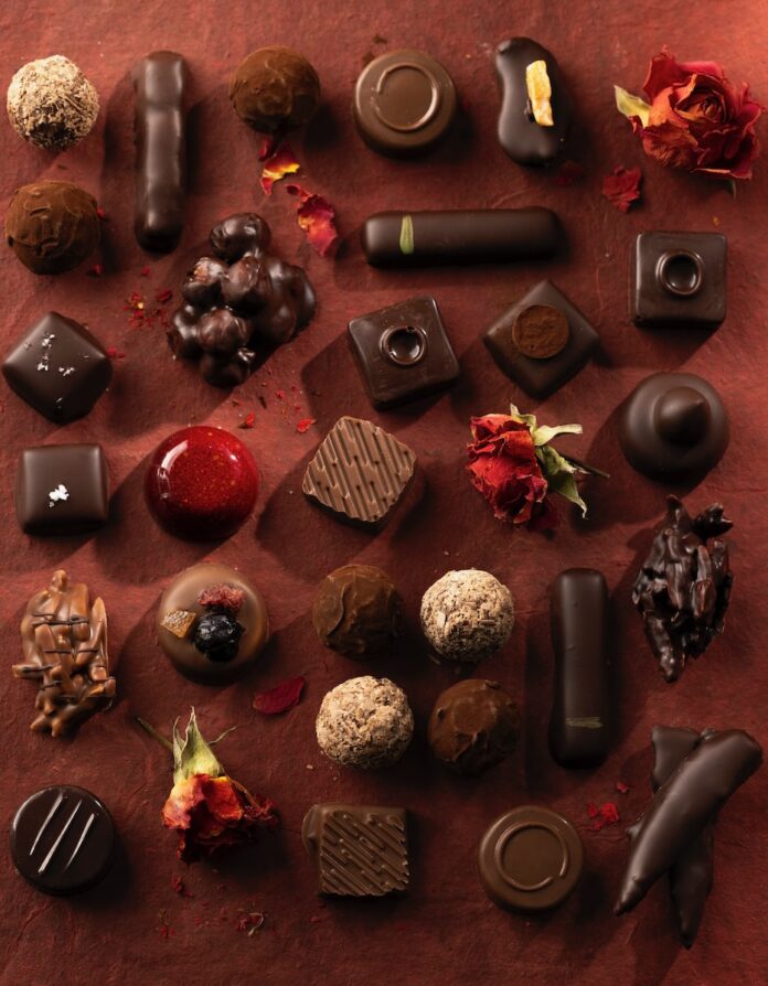Various truffles and chocolates in white dark and milk lay out on an orange table.