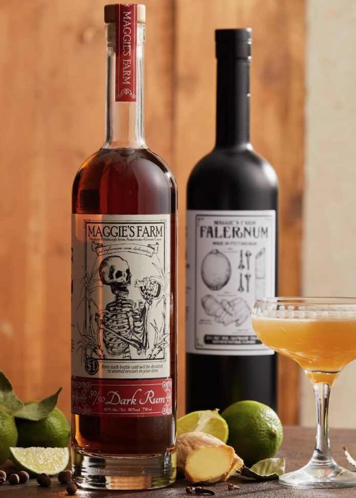 Two bottles from Maggie's Farm Distillery in Pittsburgh sit on a table beside a tall cocktail.