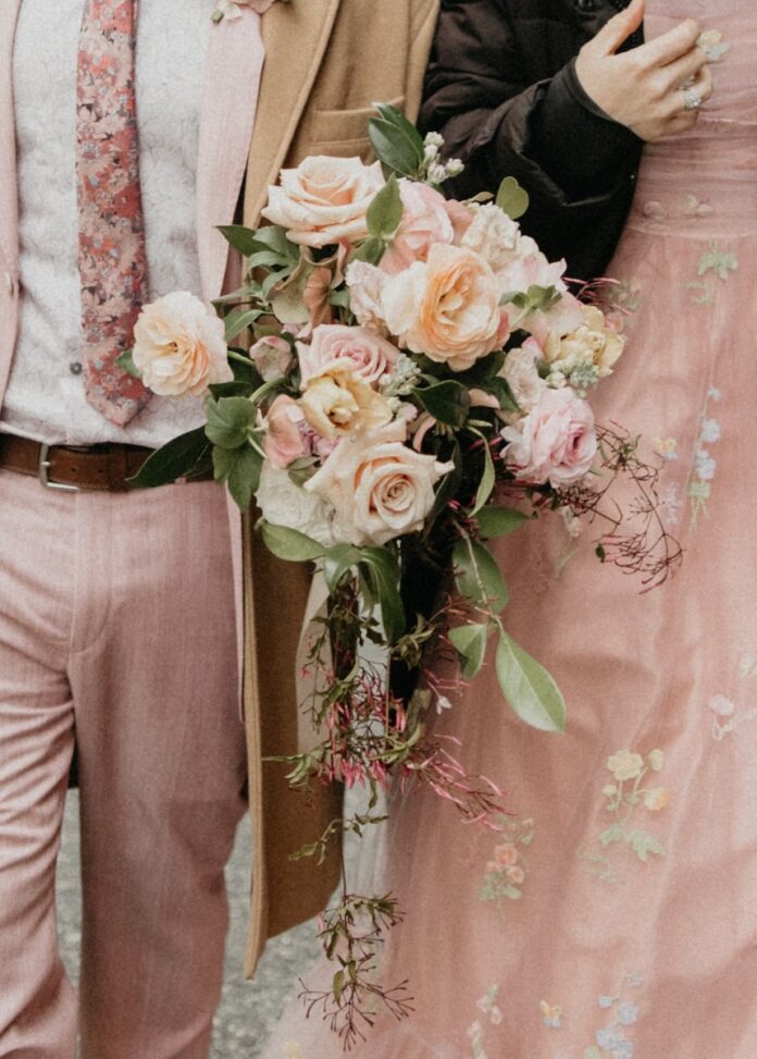 A woman and man walk with a bouquet of pink flowers between them.