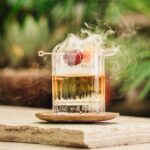 Smoked Old Fashioned with cherry garnish and greenery in the background