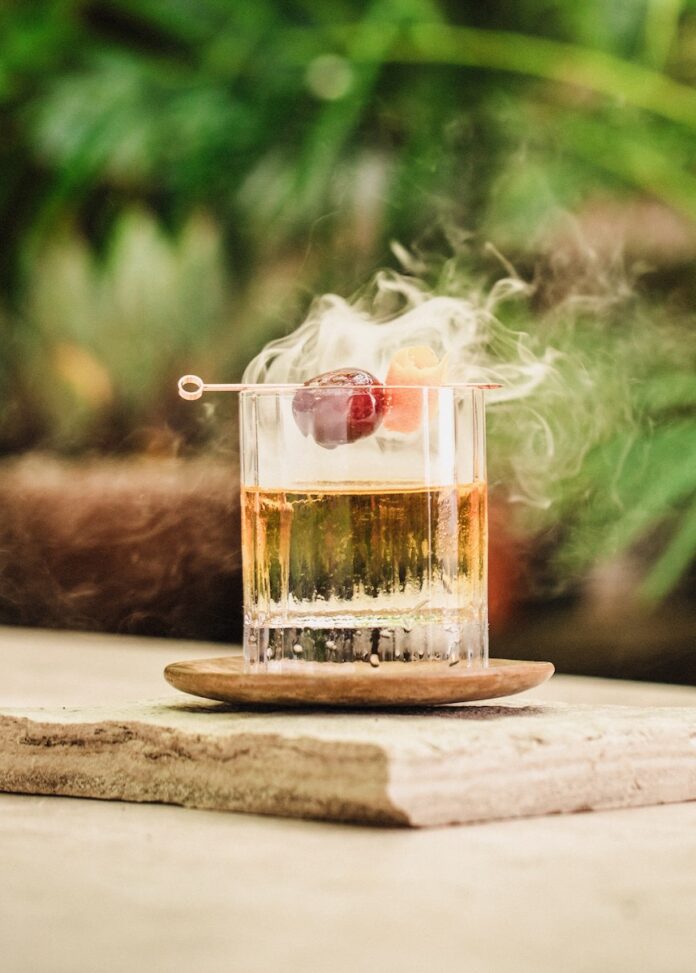 Smoked Old Fashioned with cherry garnish and greenery in the background