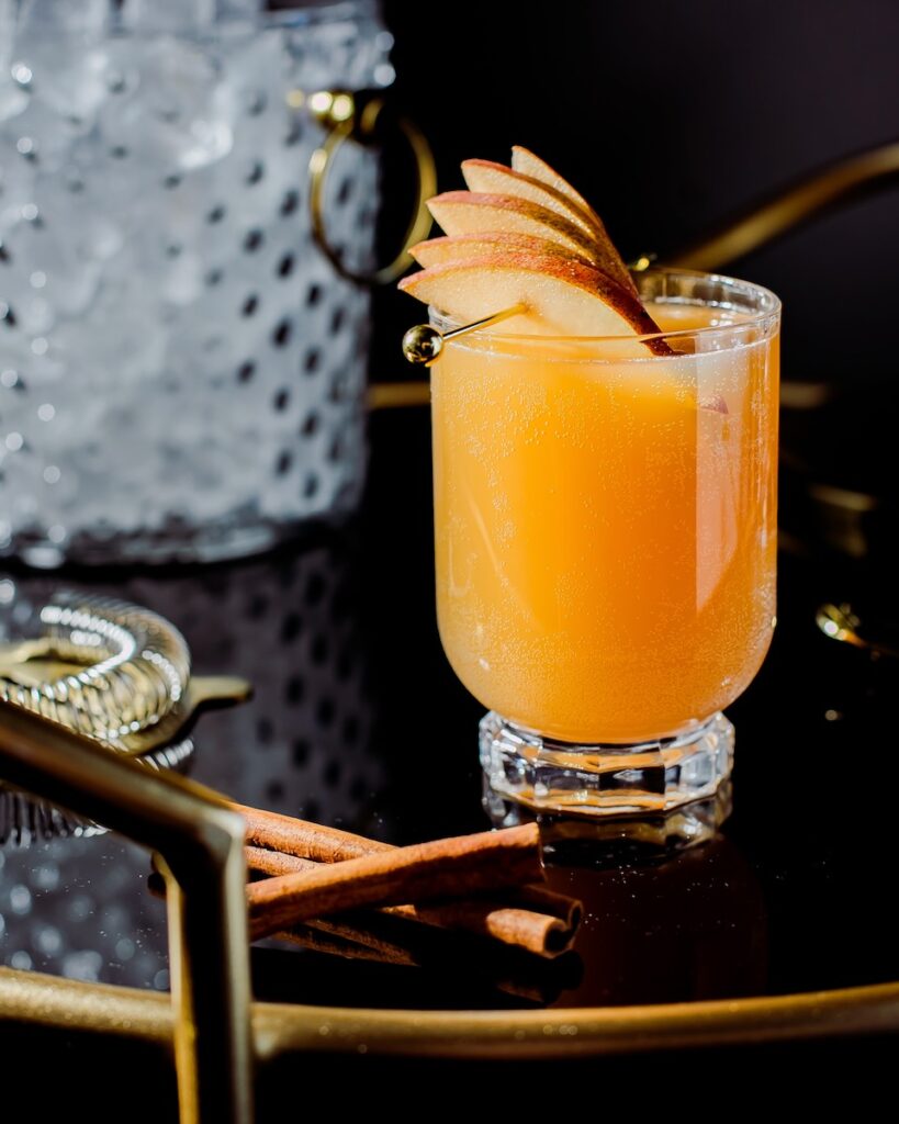An orange mocktail garnished with pear sits on a black bar cart, looking inviting and delicious