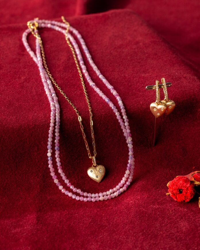 A pink bead necklace and gold heart locket sit on a red table.