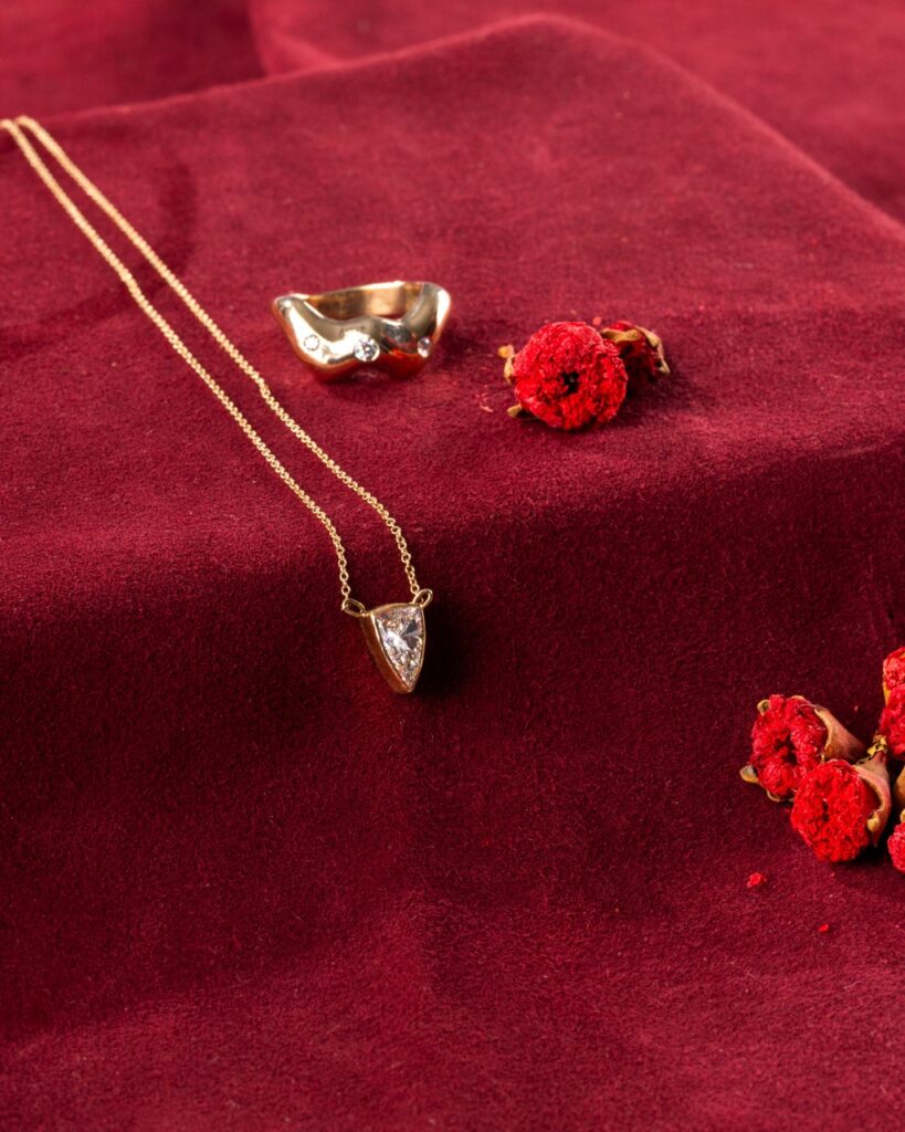 A dainty gold necklace hands over a red table.