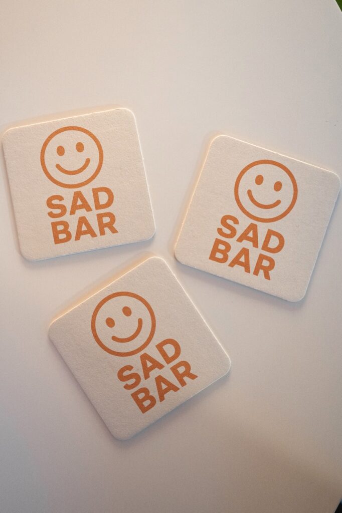 Three Sad Bar coasters sit on a white table.