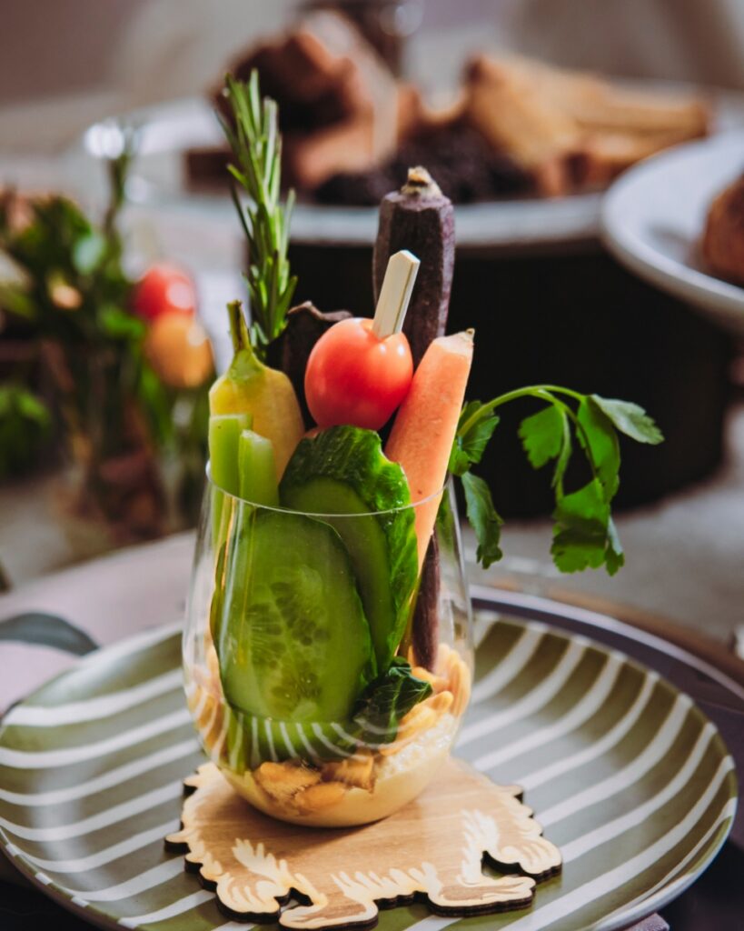 A colorful crudité appetizer served in a stemless acrylic wine glass featuring cucumber, carrots, and tomatoes at a themed children's party.