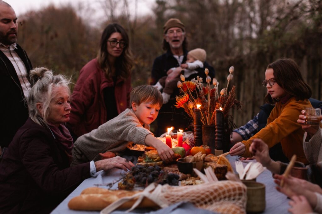 A multi-generational family and friends gathered around a candlelit outdoor table for a rustic autumn feast at dusk near Pittsburgh.