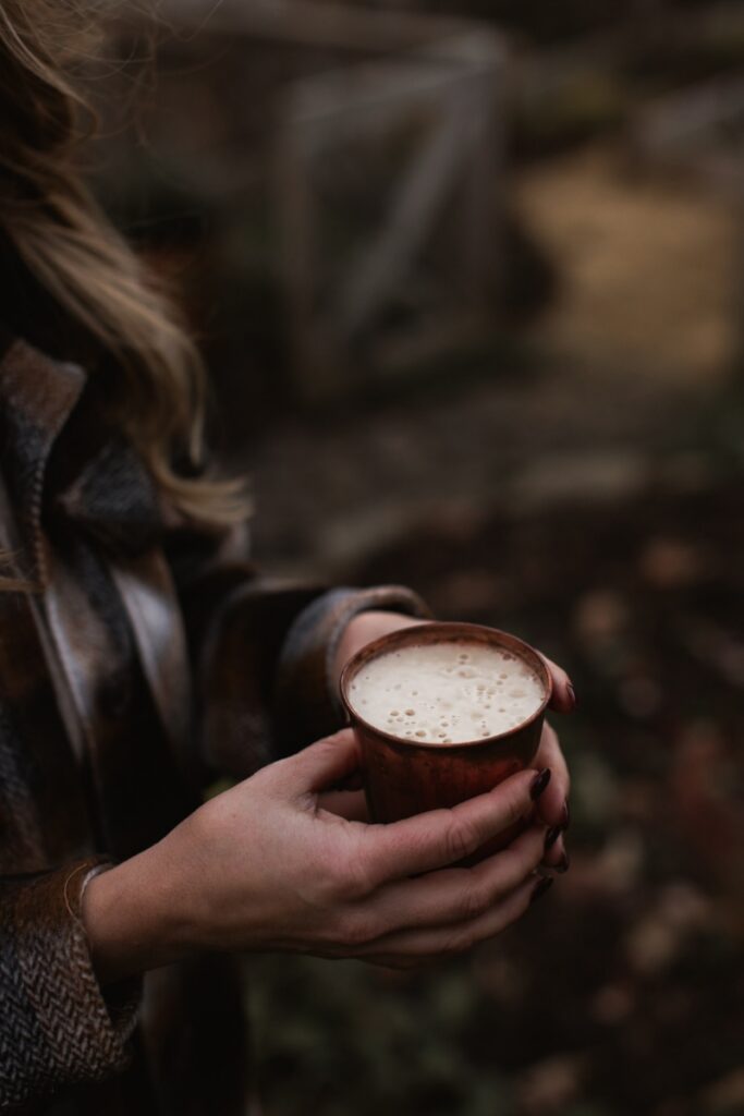 A person in a plaid jacket holding a frothy drink in a copper mug during a sunset outdoor gathering.