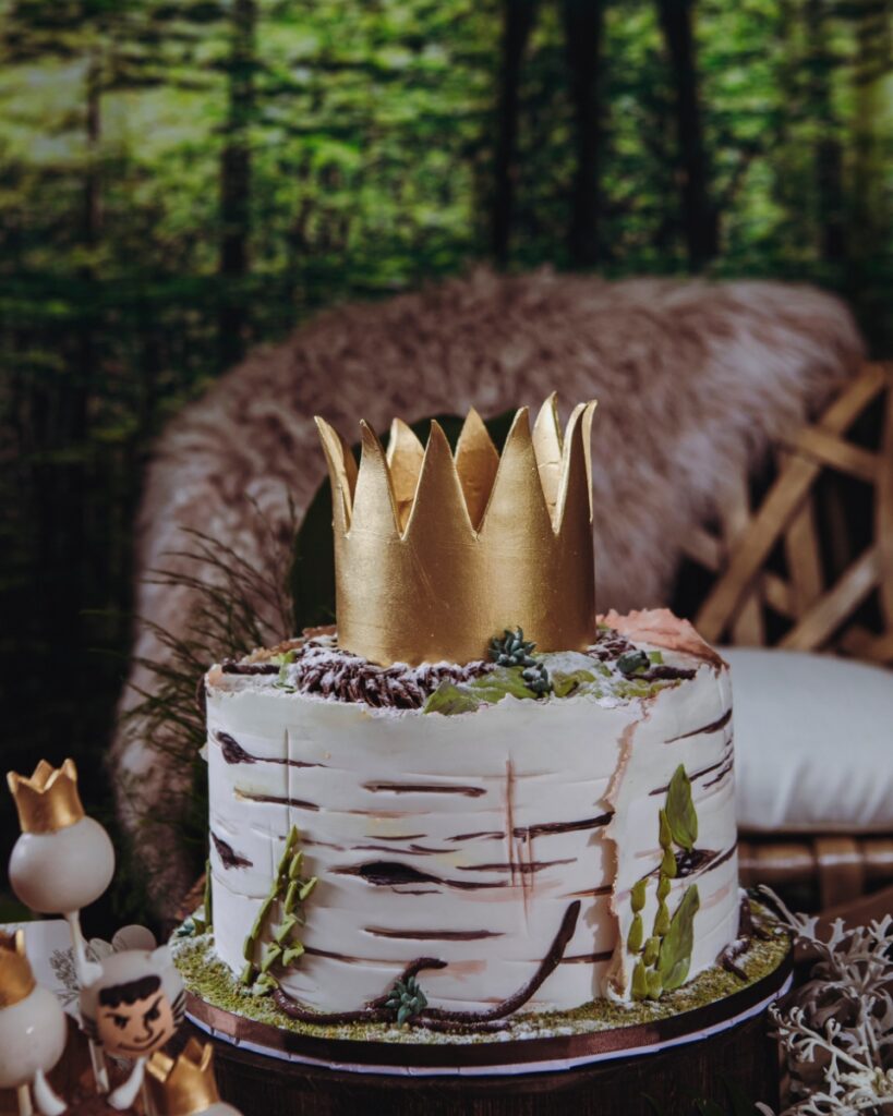 A tiered layer cake decorated to look like a birch tree trunk topped with a gold crown, featured at a "Where the Wild Things Are" themed birthday party.