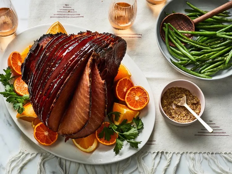 An. apple cider ham on a white background with green beans on the side.