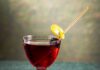 Artist in Residence (Chocolate Cherry Negroni) Artist in Residence cocktail in a stemmed glass, garnished with a Luxardo cherry wrapped in a lemon twist, featuring flavors of citrus gin, cherry, and chocolate bitters.