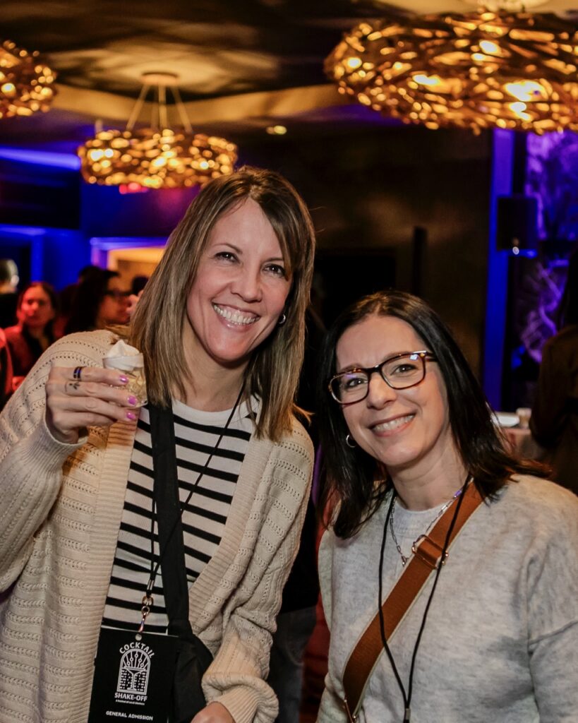 Two women smile with small cocktails.