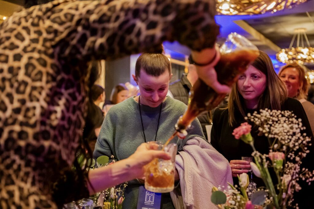 A woman pours a cocktail into a glass.