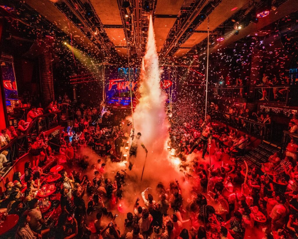 A packed dance floor with steam coming down from the middle of the ceiling.