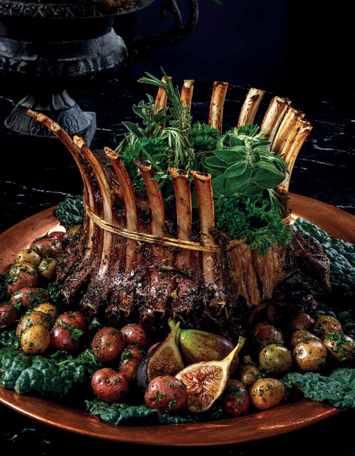 A crown roast of lamb with min sauce from the gilded age sits among a bed of figs and potatoes and greens.