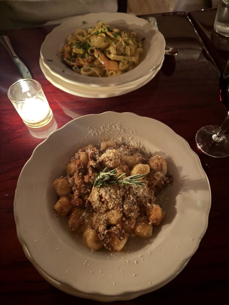 Two white bowls full of pasta with candlelight in between them.